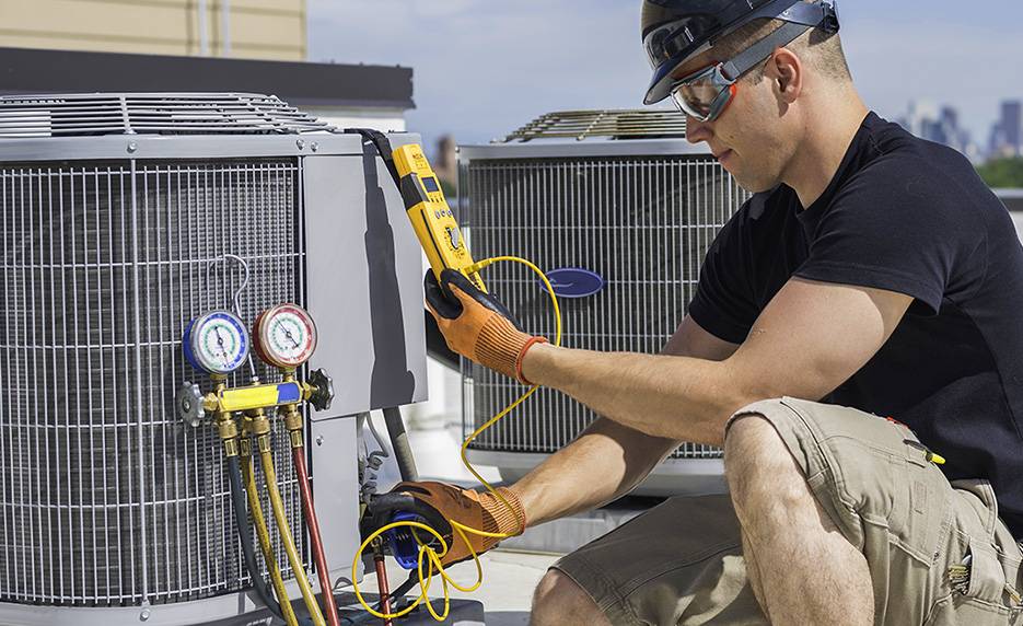 Skilled Heatwave HVAC technician, wearing protective goggles and gloves, performing AC repair, checking and servicing components for optimal functionality.