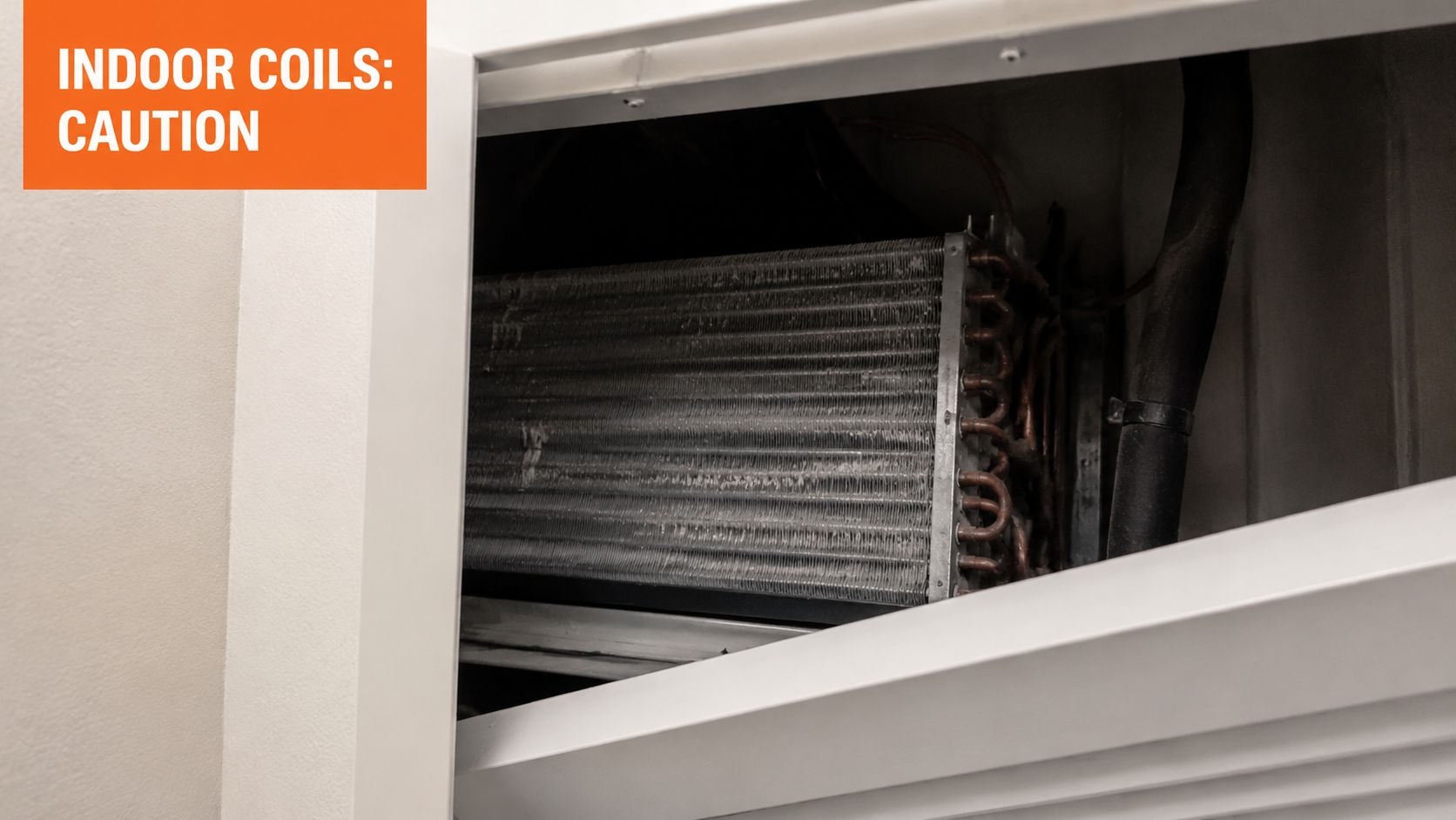 A close up view of dirty indoor air conditioning coils exposed inside an open HVAC unit housing.